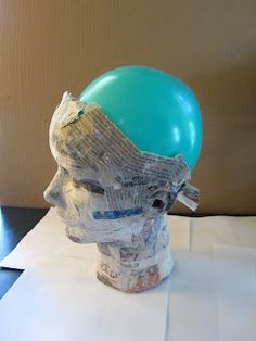 a paper mache head with a blue balloon on it's side sitting on top of a piece of white paper