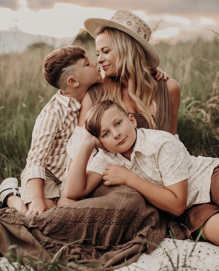 a woman and two boys are sitting on the ground with their arms around each other