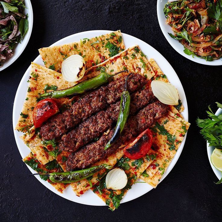 several plates of food are arranged on a black tablecloth, including meats and veggies