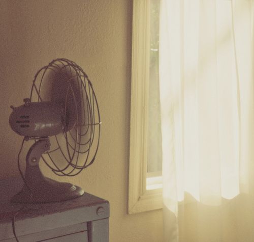 an old fan sitting on top of a table next to a window with the sun shining through it