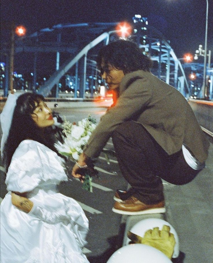 a man kneeling down next to a woman in a wedding dress on a skateboard