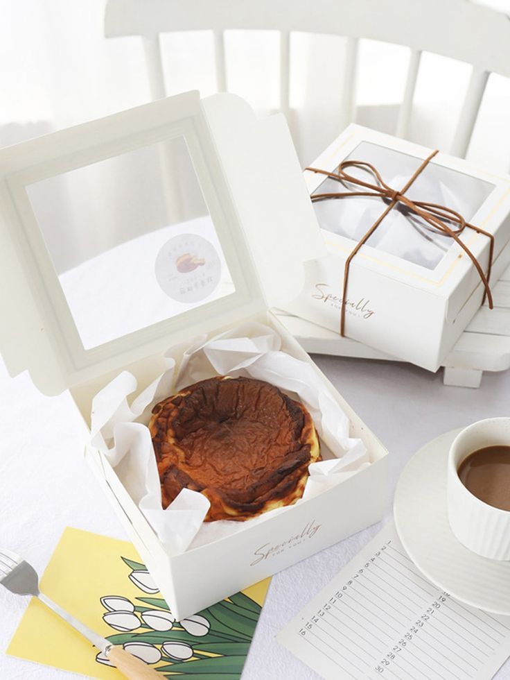 a cup of coffee sitting next to a pastry in a box on top of a table