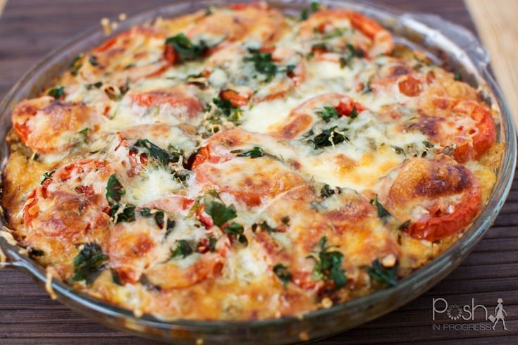 a close up of a pizza in a pan on a wooden table with cheese and spinach