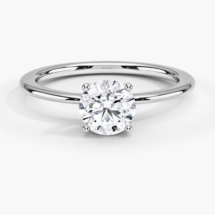 a white gold engagement ring with a round brilliant cut diamond in the center, on a plain surface