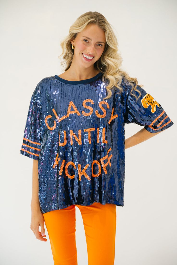 This CLASSY UNTIL KICKOFF TIGER SEQUIN TOP is the perfect way to show school spirit for the big game. Featuring a mix of navy and orange, this top let's you represent your team in style with a tiger patch accent on the sleeve. You'll be sure to stand out on gameday. All orders are currently shipping within 14 business days. To receive item quicker, expedited shipping is available at checkout. Varsity Tops For Cheerleading During Football Season, Orange Team Spirit Sports Top, Collegiate Blue Tops For Cheerleading, Orange Crew Neck Top For Sports Season, Navy Short Sleeve Tops For Fall, Orange Team Spirit Tops For Sports Events, Varsity Team-colored Tops For Game Day, Blue Sports Fan Tops For Football Season, Blue School Spirit Tops For College