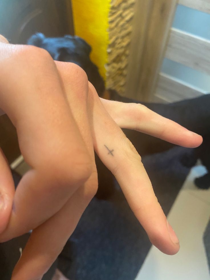 a person's hand with a small cross tattoo on the middle finger, sitting next to a black dog