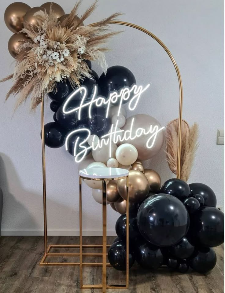 a happy birthday sign surrounded by black and gold balloons