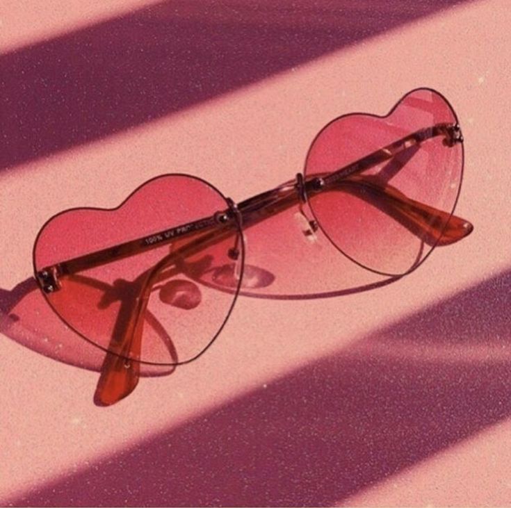 a pair of heart - shaped sunglasses sitting on top of a pink surface with long shadows