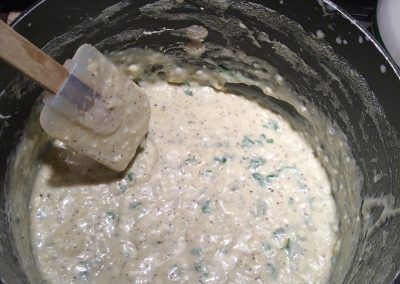 a wooden spatula mixing batter in a black pot on top of a stovetop