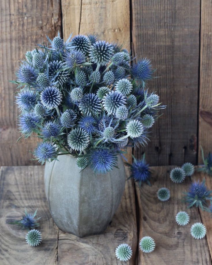 an arrangement of blue flowers in a vase on a wooden table next to wood planks