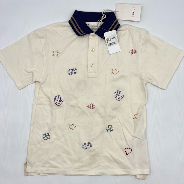 Gucci Celebrates Its Many Famous Motifs On This Polo Shirt, Embroidering The Ivory Piqu Piece With A Repeated Pattern Of Bees, Lucky Clovers, Stars, Hearts And, Of Course, The Fashion House’s Iconic ‘G’s. It’s Expertly Crafted In Italy From A Stretchy Cotton Blend And Fitted With A Contrasting, Twin-Tipped Navy Collar. 93% Cotton, 7% Elastane Piqu Fabric 2-Button Placket Made In Italy Gucci Long Sleeve Tops With Embroidered Logo, Gucci Cotton Polo Collar Top, Gucci Cotton Collared Top, Gucci Collared Cotton Tops, Casual Multicolor Gucci Tops, Gucci Cotton Tops For Spring, Designer Gucci Tops For Spring, Designer Embroidered Collared Tops, Designer Embroidered Summer Tops