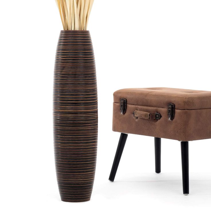 a tall vase sitting next to a footstool with sticks sticking out of it