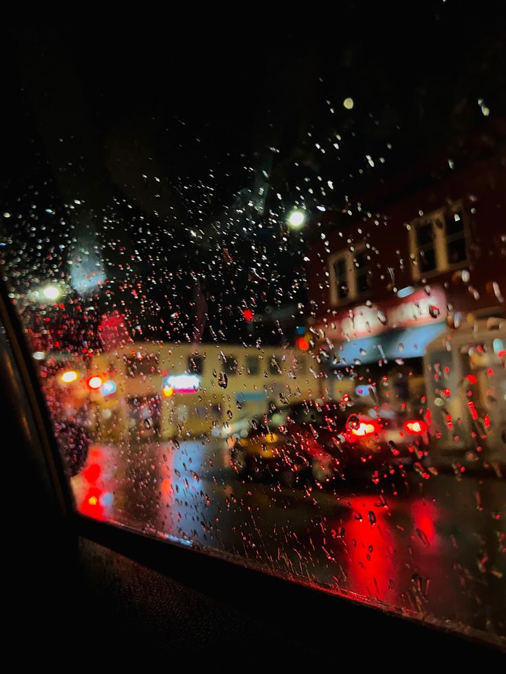 rain is pouring down on the window and cars are parked in the street at night