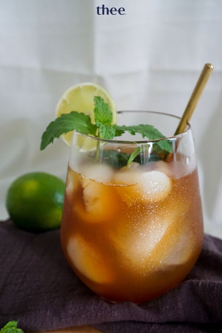 a glass filled with ice and mint on top of a purple cloth next to limes