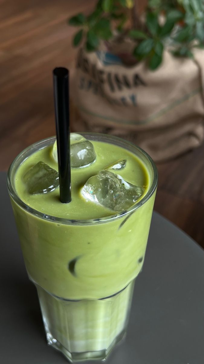 a green drink with ice cubes and a black straw in the middle on a table