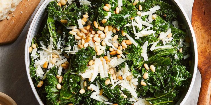 a bowl filled with greens and nuts next to bread