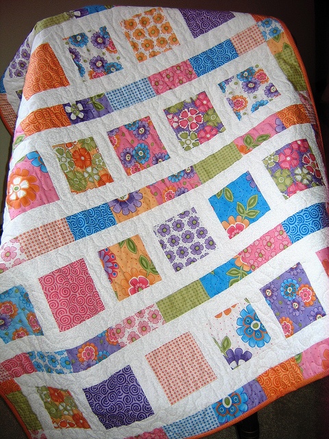 a colorful quilt is on top of a wooden chair and it has flowers all over it