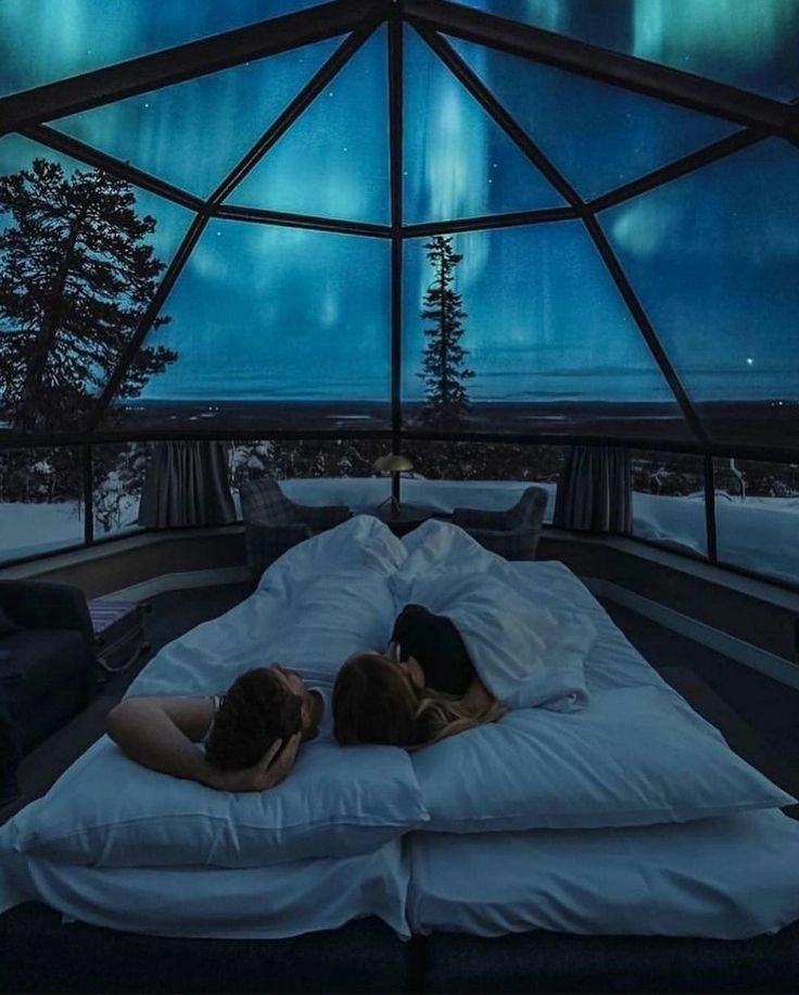 two people are laying in bed under the stars and northern lights, with their backs to each other