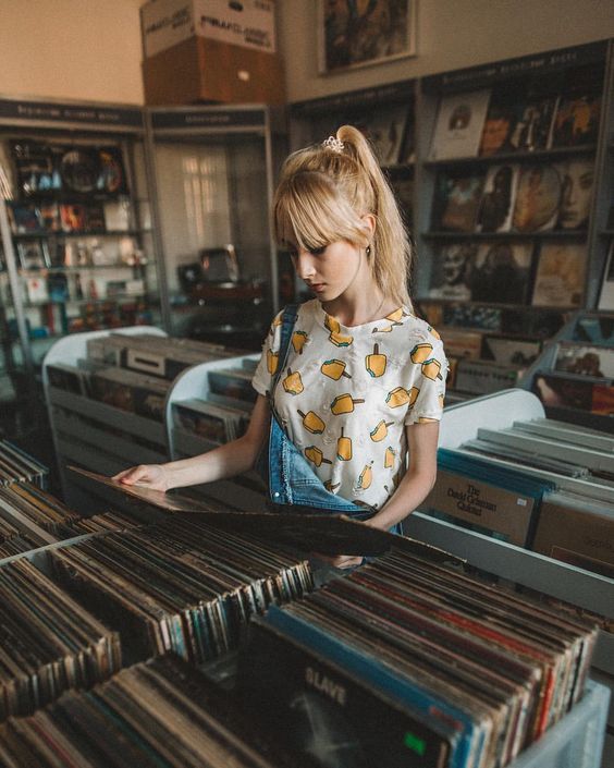 a woman is looking through records in a record shop with many stacks of records on the shelves