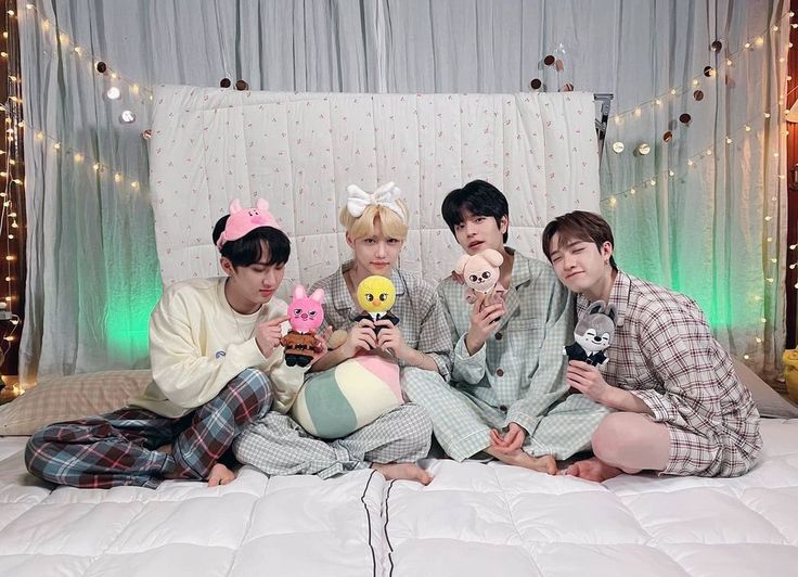 four people sitting on a bed holding stuffed animals