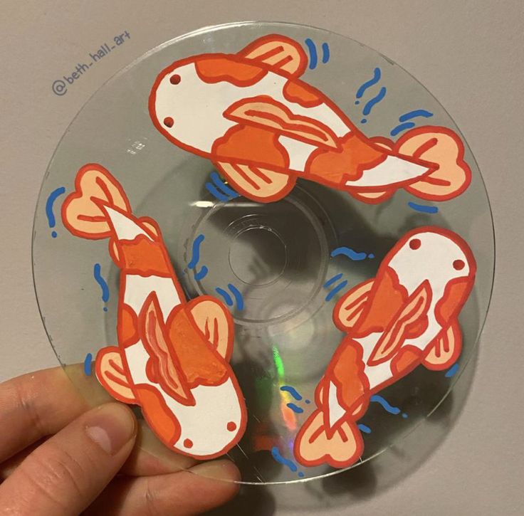 a hand holding a clear disc with orange and white fish on it