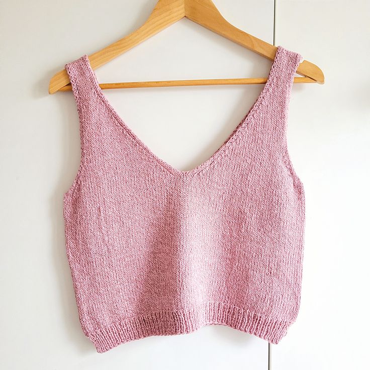 a pink crop top hanging up on a wooden hanger next to a white wall