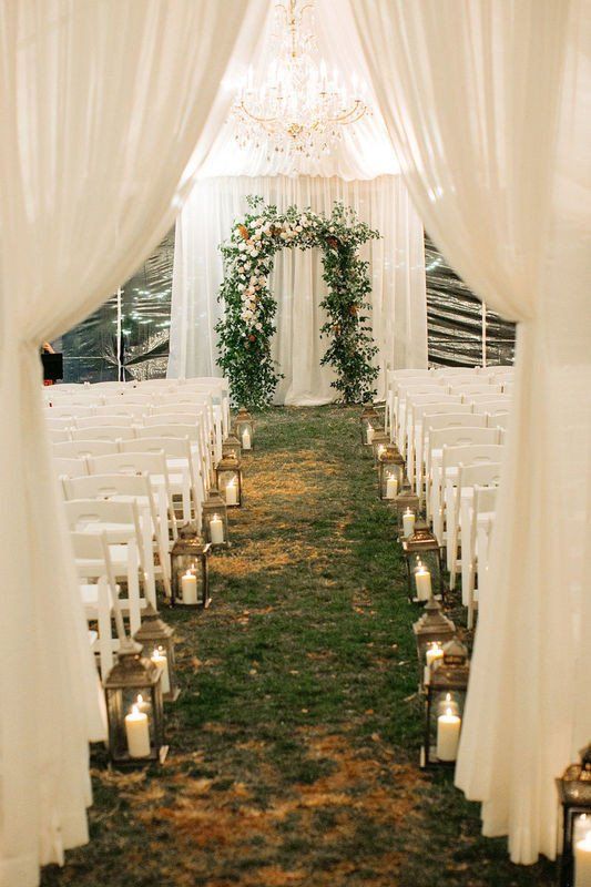 the aisle is lined with candles and white drapes for an outdoor wedding ceremony at night