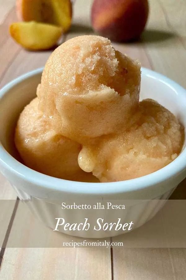 a white bowl filled with peach sorbet next to two pieces of peaches