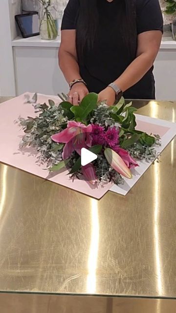 a woman standing in front of a table with flowers and greenery on top of it