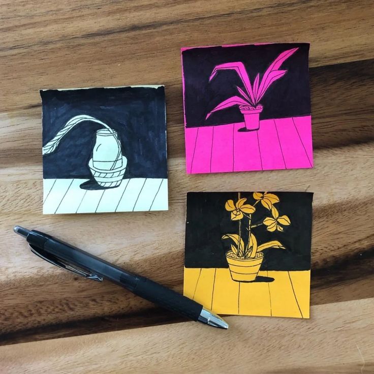 three different colored paintings on top of a wooden table next to a pen and paper