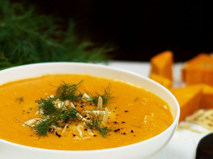 a white bowl filled with carrot soup and garnished with parmesan cheese