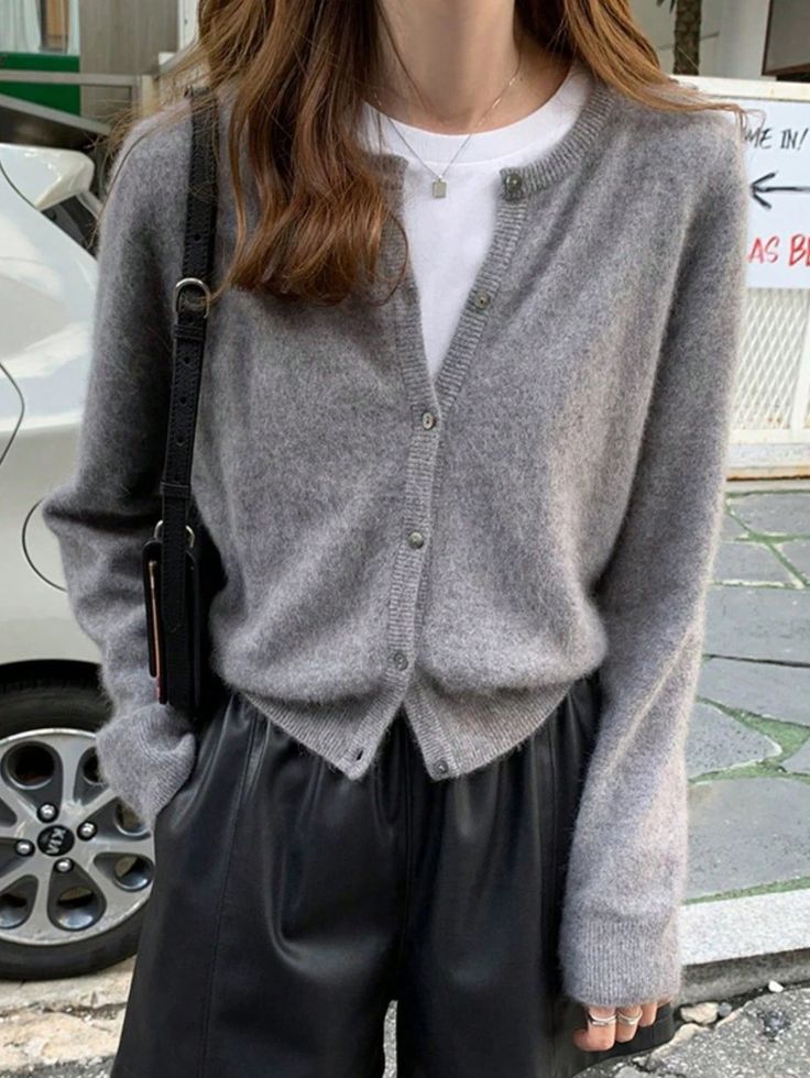 a woman wearing black leather shorts and a gray cardigan sweater is standing on the street