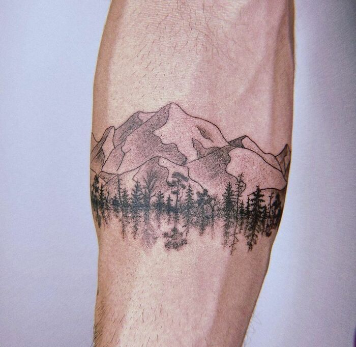 a man's arm with a mountain and forest tattoo on the left side of his leg