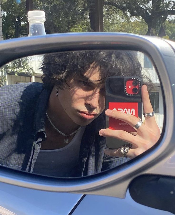 a man taking a selfie in the side mirror of a car with his cell phone