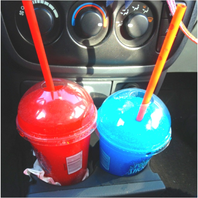 two plastic cups sitting next to each other in front of a car dashboard with orange and blue straws sticking out of them