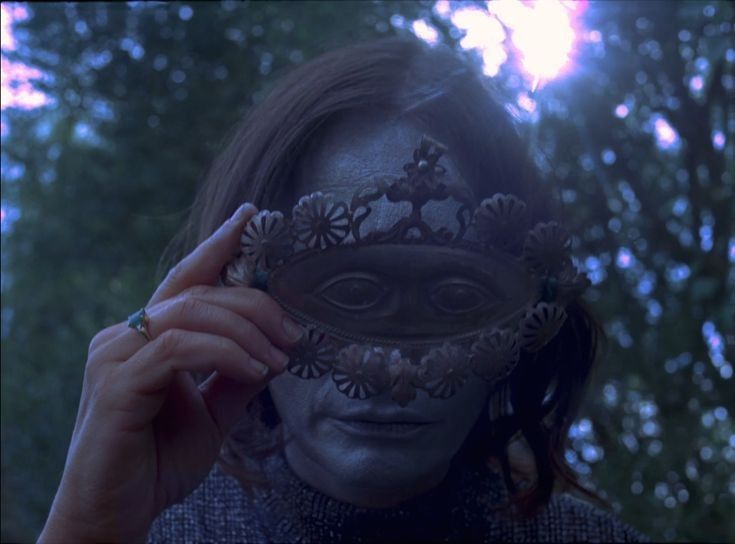 a woman with her face painted in silver and holding a mask over her eyes to the side