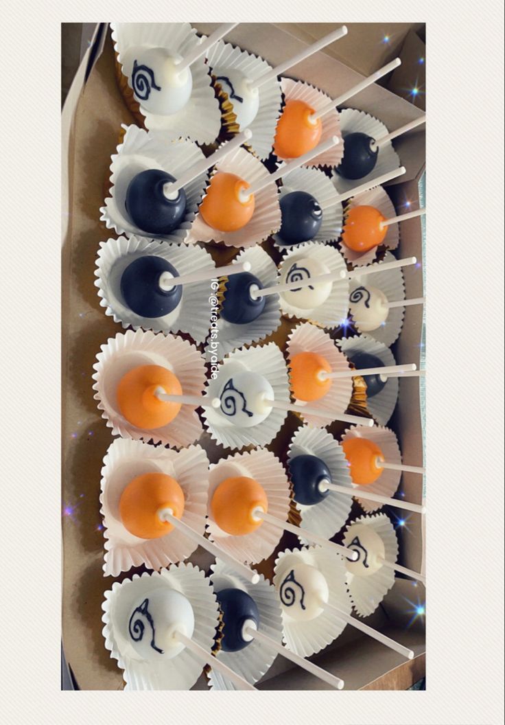 there are many cupcakes with orange and blue toppings on sticks in the box