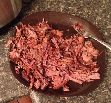 shredded meat on a plate with a fork and crock pot in the back ground