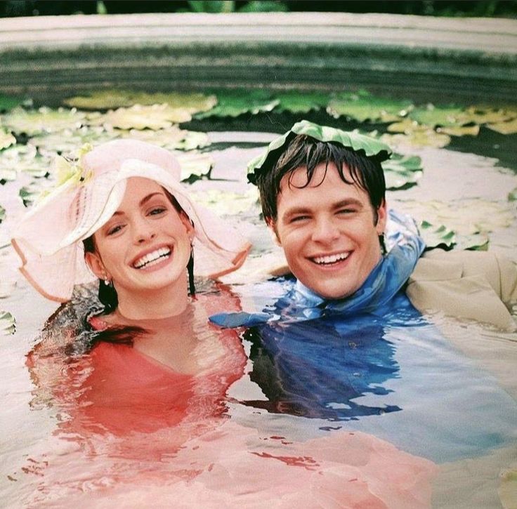 a man and woman are in the water with hats on their heads, smiling at the camera