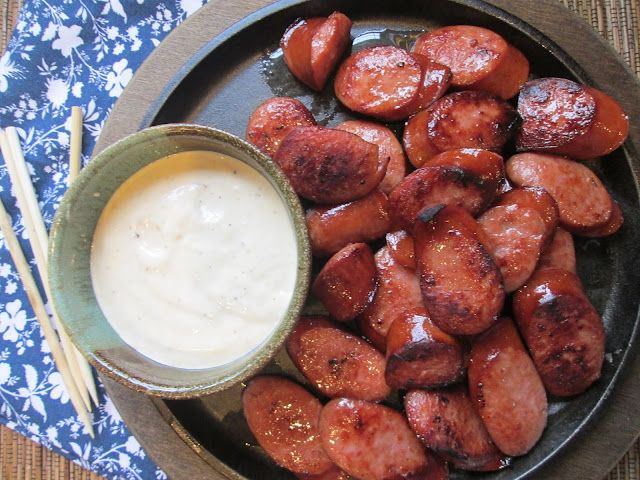 a plate full of cooked sausages next to a bowl of ranch dressing with chopsticks on the side