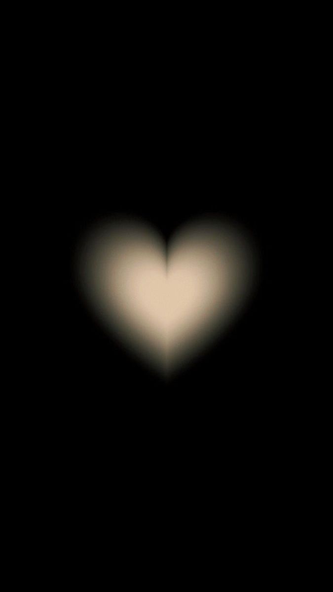 a blurry image of a white heart in the middle of black background with light coming from it