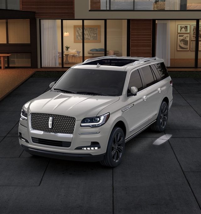 a white suv parked in front of a house at night with the door open and windows lit up