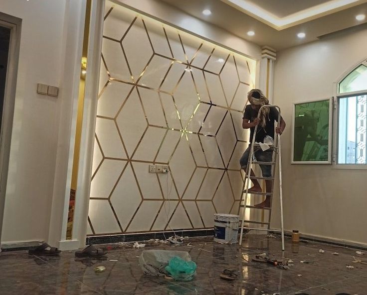 a woman is standing on a ladder in front of a wall with gold geometric designs