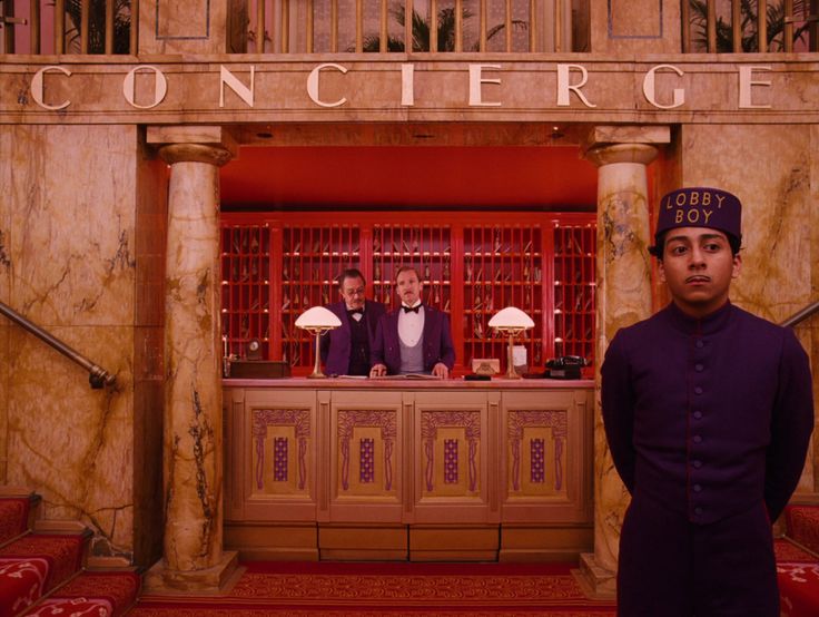 three men in tuxedos stand at the front of a hotel lobby bar with red walls