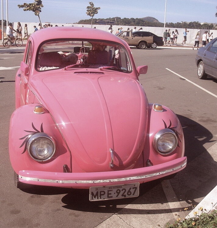 an old pink beetle parked in a parking lot