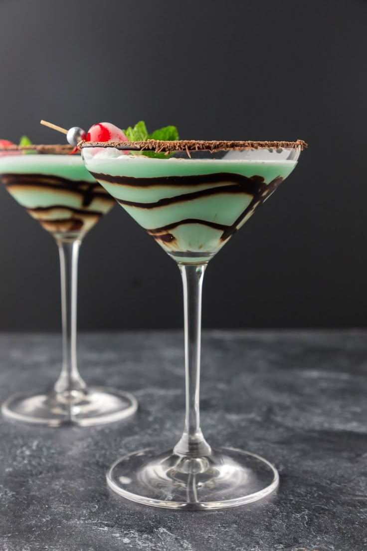 two martini glasses filled with green liquid and garnished with cherries on the rim