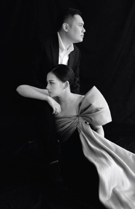 a man and woman sitting next to each other in front of a black background with white sheets