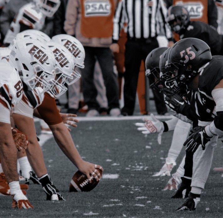 a group of football players kneel down on the sidelines during a game as an official looks on