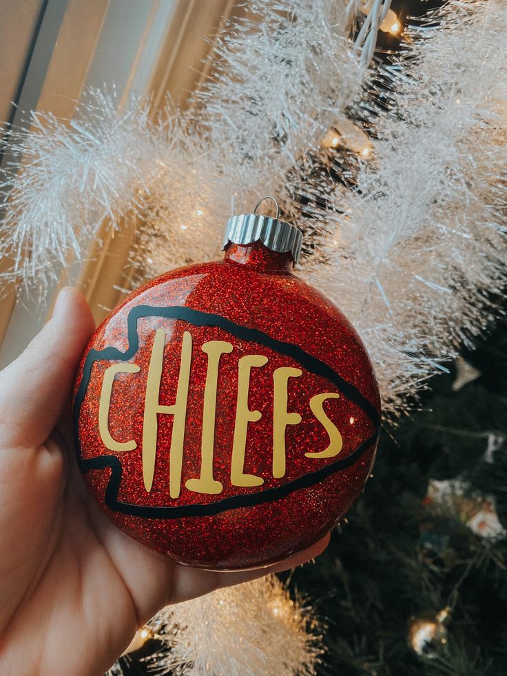 a hand holding a red ornament with the word chiefs on it in front of a christmas tree