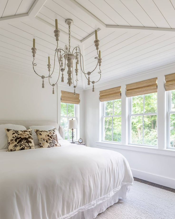 a white bedroom with chandelier and windows